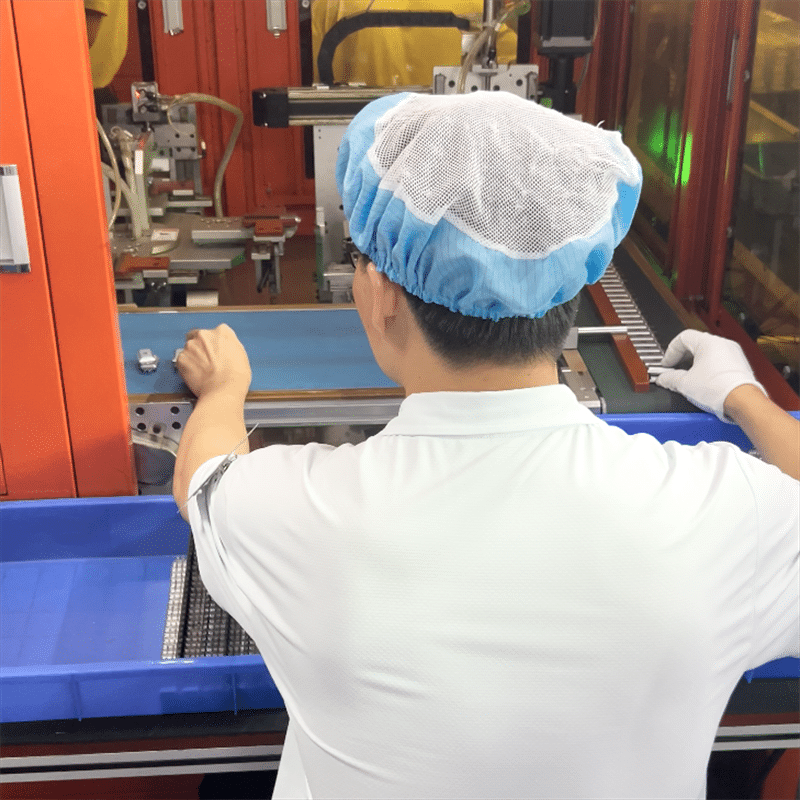worker operating automated production machine for heating elements in heated clothing factory assembly line