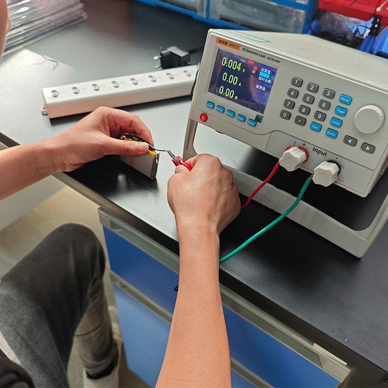 technician testing rechargeable battery pack for heated clothing electric heating system performance and safety