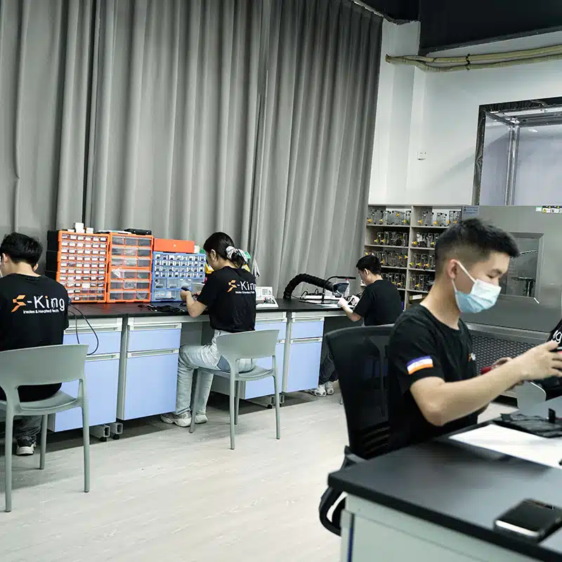 engineers working on heated clothing electronic components and heating system assembly in R&D workshop