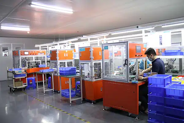 Inside a modern battery manufacturing facility, showing technicians and automated assembly lines producing and testing lithium-ion battery packs for heated clothing applications.