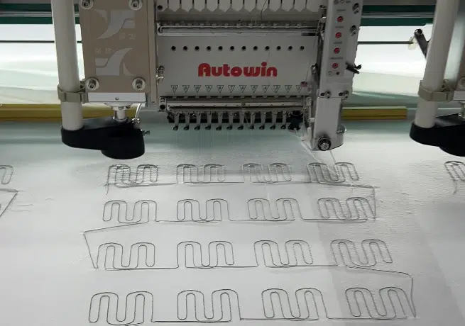 Industrial automatic embroidery machine processing fabric for custom heated gloves, showing high-precision manufacturing of heated gloves at our factory